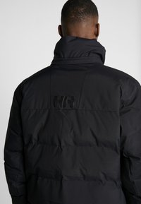 Black padded jacket with a high collar, featuring a textured finish and a subtle brand logo on the back.