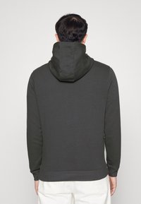 Sudadera gris oscura con una gran capucha doblada, puños acanalados y dobladillo recto. Textura suave y diseño informal. Vista desde la parte posterior.