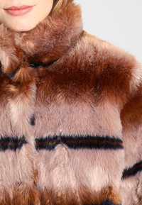 Brązowa kurtka z imitacji futra, charakteryzująca się miękką, puszystą fakturą, pionowymi czarnymi paskami i wysokim kołnierzem.