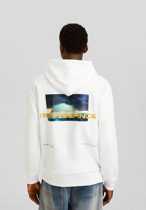 Person trägt einen weißen Hoodie mit einer bunten, stürmischen Himmel-Grafik und dem Schriftzug "RENAISSANCE" auf dem Rücken, kombiniert mit blauen Jeans.