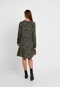 Černé a olivově zelené šaty se zvířecím potiskem, dlouhými rukávy, rozšířenou sukní a volným střihem, s kulatým výstřihem a lehkou látkou.