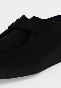 Μαύρα παπούτσια slip-on με στρογγυλεμένη μύτη και υφασμένη λωρίδα στην κορυφή, με χοντρή λαστιχένια σόλα.