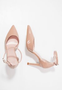 Nude lakované lodičky na vysokém podpatku s špičatou špičkou a řemínkem kolem kotníku, s hladkým povrchem a štíhlým jehlovým podpatkem.