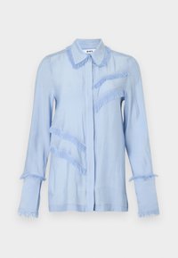 Γαλάζιο μακρυμάνικο μπλουζάκι με διακοσμητικά κρόσσια κατά μήκος του γιακά, των μανσετών, στο μπροστινό μέρος στο στήθος και διαγώνιες γραμμές στην αριστερή πλευρά.