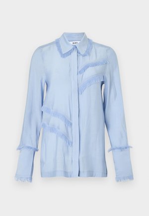 Svijetloplava bluza dugih rukava s resicama oko ovratnika, manšeta, prednjeg dijela prsa i dijagonalnih linija na lijevoj strani.