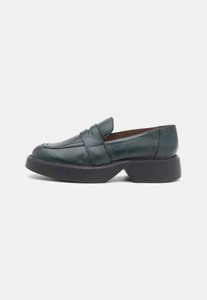 Mocassins en cuir vert foncé avec un petit talon bloc, présentant un design élégant, des détails cousus et un bout arrondi.