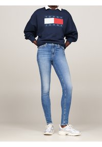 Laivaston huppari, jossa on valkoinen kaulus ja punavalkoinen logo; vaaleansiniset kapeat farkut; valkoiset ja harmaat lenkkarit. Suorat tekstuurit, rento muotoilu.