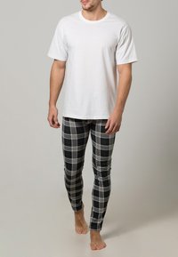 Camiseta blanca de algodón combinada con leggings ajustados de cuadros grises con acentos en negro y azul. El modelo está descalzo frente a un fondo neutro.