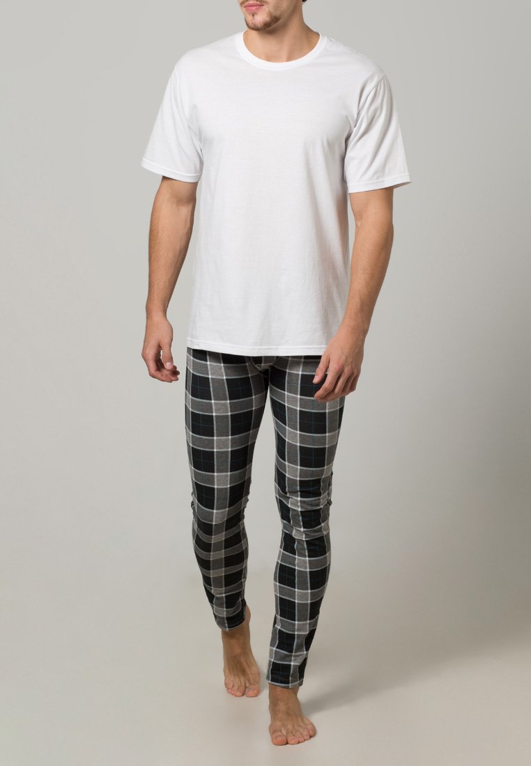 Camiseta blanca de algodón combinada con leggings ajustados de cuadros grises con acentos en negro y azul. El modelo está descalzo frente a un fondo neutro.