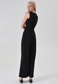 Combinaison noire sans manches avec un corsage ajusté et une silhouette à jambes larges, présentant une texture lisse et un design minimaliste.