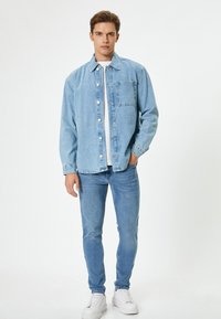 Chaqueta de mezclilla de color azul claro con bolsillo frontal, botones blancos y un acabado texturizado, combinada con jeans skinny azul claro y zapatillas blancas.