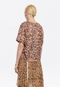 Leopard print top in lightweight fabric, short sleeves, round neckline, paired with a matching tiered skirt, both showcasing earthy tones.