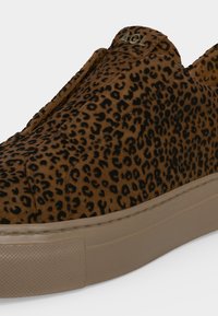 Baskets avec tige imprimé léopard marron et noir et semelle en caoutchouc beige avec petit logo métallique AGL près du bord supérieur.