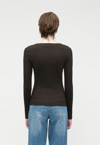 Μακρυμάνικο ribbed μπλουζάκι σε σκούρο καφέ, με σχήμα πλοίου στο λαιμό και εφαρμοστή γραμμή. Συνδυάζεται με ανοιχτό μπλε ψηλόμεσο τζιν.