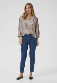 Animal print top in beige and brown, with a V-neck and puffed sleeves; paired with blue skinny jeans and black flats.