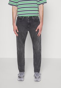 Jeans neri in denim con vestibilità comoda, cinque tasche e leggero effetto scolorito. Abbinati a una maglietta a righe verde e nera e a sneakers grigie.