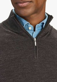 Tumma harmaa vetoketjullinen villapaita, jossa on korkea kaulus. Paidassa on hopeinen vetoketju ja sen alla vaalea sininen kauluspaita. Pinta on sileää neulosta.