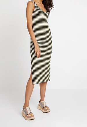 Femme portant une robe midi sans manches à rayures noir et blanc avec une fente latérale, associée à des baskets épaisses multicolores.