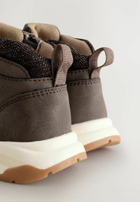 Graue Turnschuhe mit einem strukturierten Leder-Obermaterial, sandfarbenen Mesh-Akzenten und Zuglaschen, ausgestattet mit einer weißen Midsol und Gummi-Außensohle.