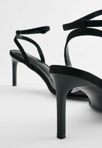 Sandali neri in suede con tacco alto, design minimalista e cinturini incrociati alla caviglia. Soletta piatta e interno nero liscio.