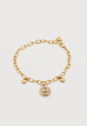 Bracelet chaîne en or avec breloques en forme de cœur et un pendentif rond arborant un "G" entouré de petits cristaux et le mot "Guess".
