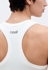 Close-up of a person’s upper back wearing a white racerback tank top with the brand name "casall" in black text.