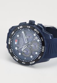 Montre chronographe bleue avec lunette noire, marqueurs numériques blancs, trois sous-cadrans, fenêtre de date et bracelet en silicone texturé.