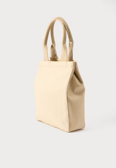 Μπεζ τσάντα ώμου με δύο επενδυμένες λαβές, ορθογώνιο σχήμα και απαλό δερμάτινο υφή, φωτογραφημένη πάνω σε ανοιχτό ουδέτερο φόντο.