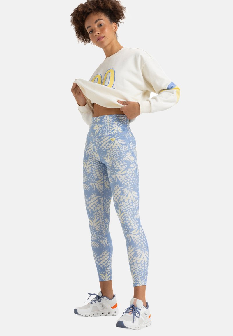 Leggings azzurri chiari con motivi floreali bianchi, design a vita alta, abbinati a una felpa crema con scollatura tonda e dettagli gialli.