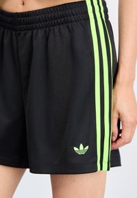 Sorte idrettsshorts med grønne vertikale striper og et brodert logo på venstre ben. Har elastisk midje og glatt stoff.