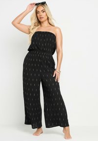 Svart axelbandslös jumpsuit med lös passform, prydd med diagonala guldlinjer, elastisk midja och vida ben.