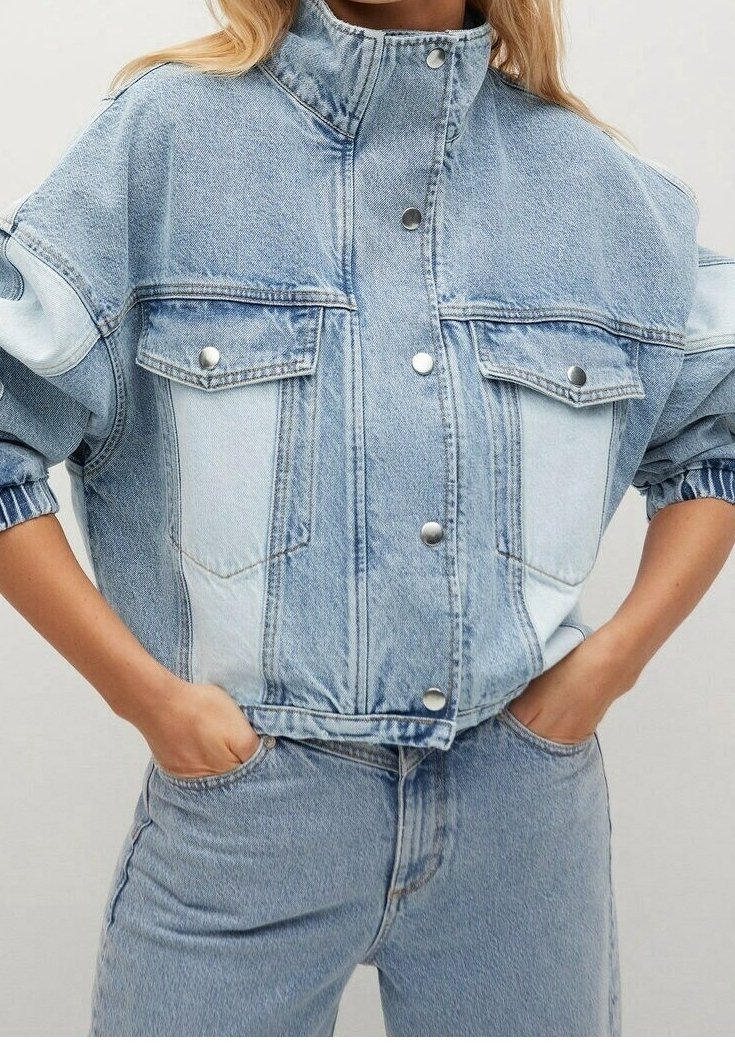 Femme portant une veste en jean bleu clair à col montant avec boutons-pression et un jean en denim assorti, mains dans les poches.