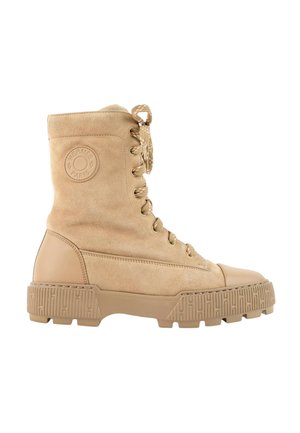 Bottine beige en daim à lacets, avec semelle épaisse texturée et patch logo rond sur le côté.