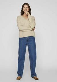 Beige v-neck sweater paired with straight-leg blue jeans. Sweater is soft-knit; jeans have a classic denim texture. Brown shoes complete the outfit.