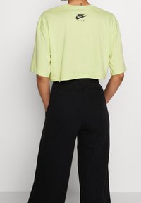 Light green cropped t-shirt made of soft fabric, featuring a black Nike Air logo on the back. Paired with black ribbed wide-leg pants.