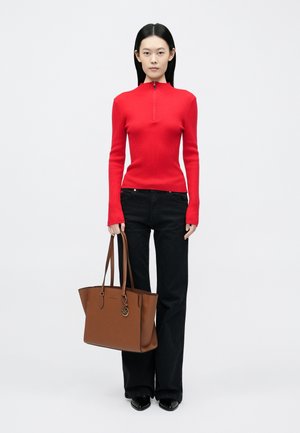 Top rojo de manga larga con costillas y un cierre alto, combinado con jeans negros acampanados. Bolso tote marrón con dos asas y detalle de logo.