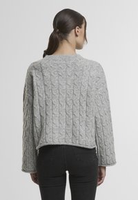 Šedý svetr s pleteným vzorem, širokým kulatým výstřihem a dlouhými rukávy. Texturovaný vzor po celém svetr ukončený nad horní částí boků.