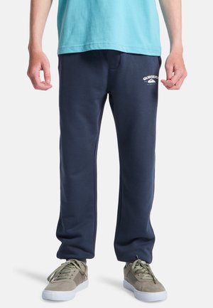 Pantalon de survêtement bleu marine en tissu doux, avec une taille à cordon et un logo blanc imprimé sur la cuisse gauche. Coupe confortable.