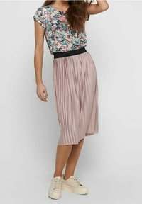 Top met bloemenpatroon en korte mouwen, gecombineerd met een geplooide, knielange roze rok en beige sneakers met een dikke zool.