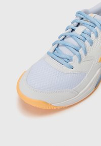 White athletic shoe with a textured mesh upper, blue laces, and an orange rubber sole. Design features a curved toe and reinforced sides.