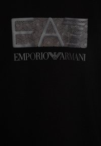 Camiseta negra con un diseño gráfico texturizado de "EA" en blanco y gris, con el logo de "Emporio Armani" debajo en letras plateadas.
