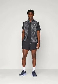 Svart og grå idrettsantrekk med en ermeløs vest, korte ermer, shorts og joggesko med hvite detaljer. Justerbar passform, sporty design.