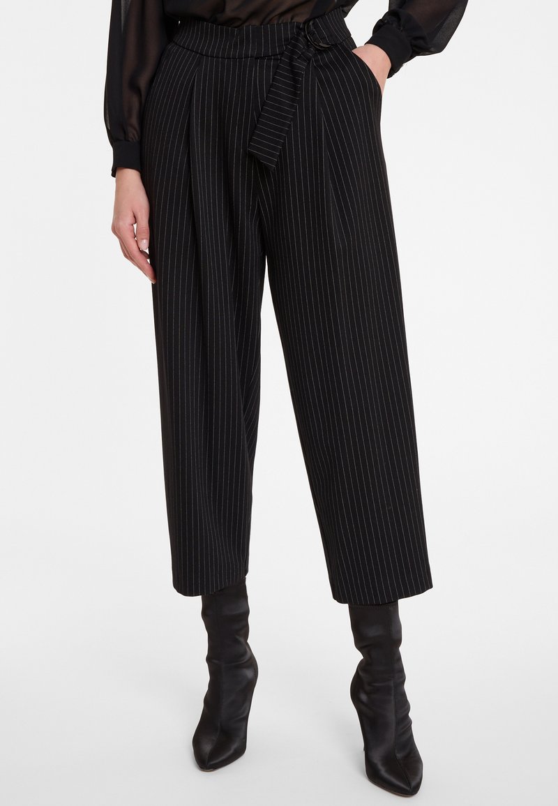 Zwart-wit gestreepte wijde broek met een ceintuur en plooien, gemaakt van een geweven stof. Gecombineerd met zwarte laarzen met hoge hakken tot de knie.