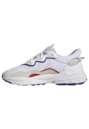 Sneaker bianco con pannelli in rete e suede, dettagli blu e rossi, suola testurizzata, forma tondeggiante e allacciatura frontale.