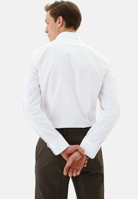 Witte langslavige shirt met een klassieke kraag en knoopdetails, in contrast met donkere geruite broeken, wat een schone, op maat gemaakte uitstraling laat zien.