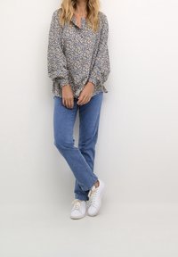 Blouse bleu clair à motifs avec des manches volumineuses, un col à patte de boutonnage, associée à un jean bleu et des baskets blanches. Tissu texturé.