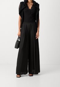 Černý žebrovaný top s krajkovým výstřihem, černý volně splývavý svetr a černé široké kalhoty. Malá černá kabelka, sandály na nízkém podpatku, minimální doplňky.