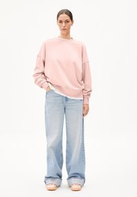 Ljusrosa oversized sweatshirt, avslappnad passform, rundad halsringning, kombinerad med ljusblå vida jeans och ljusrosa slip-on skor.