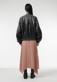 Veste bomber en cuir noir avec une taille froncée, associée à une jupe midi plissée couleur rose pâle et des bottines noires. Texture lisse sur l'ensemble.