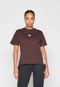 Rudas trumpų rankovių marškinėliai su baltu Adidas logotipu ant krūtinės ir baltais šonų juostelėmis, pagaminti iš minkštos medvilnės mišinys.